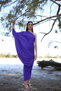 Woman in a purple dress standing by a lake with trees in the background
