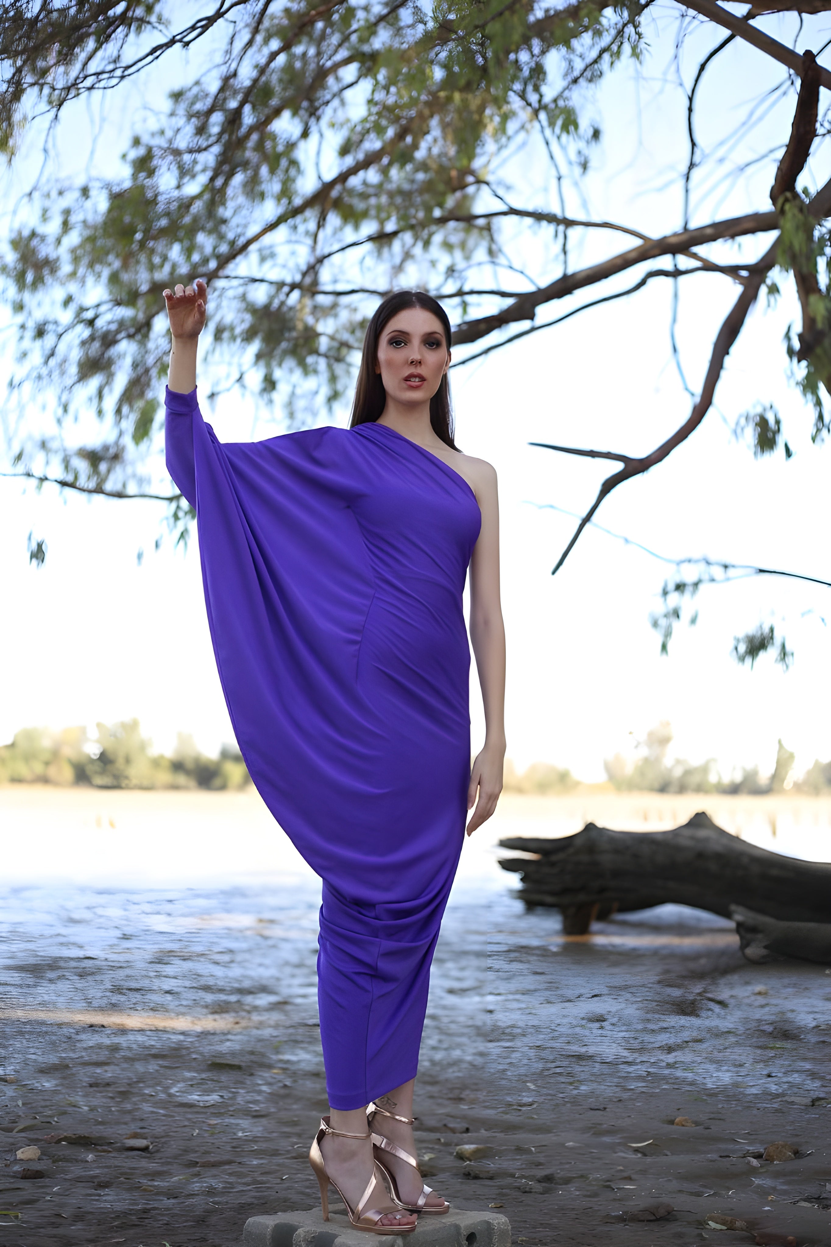 Woman in a purple dress standing by a lake with trees in the background
